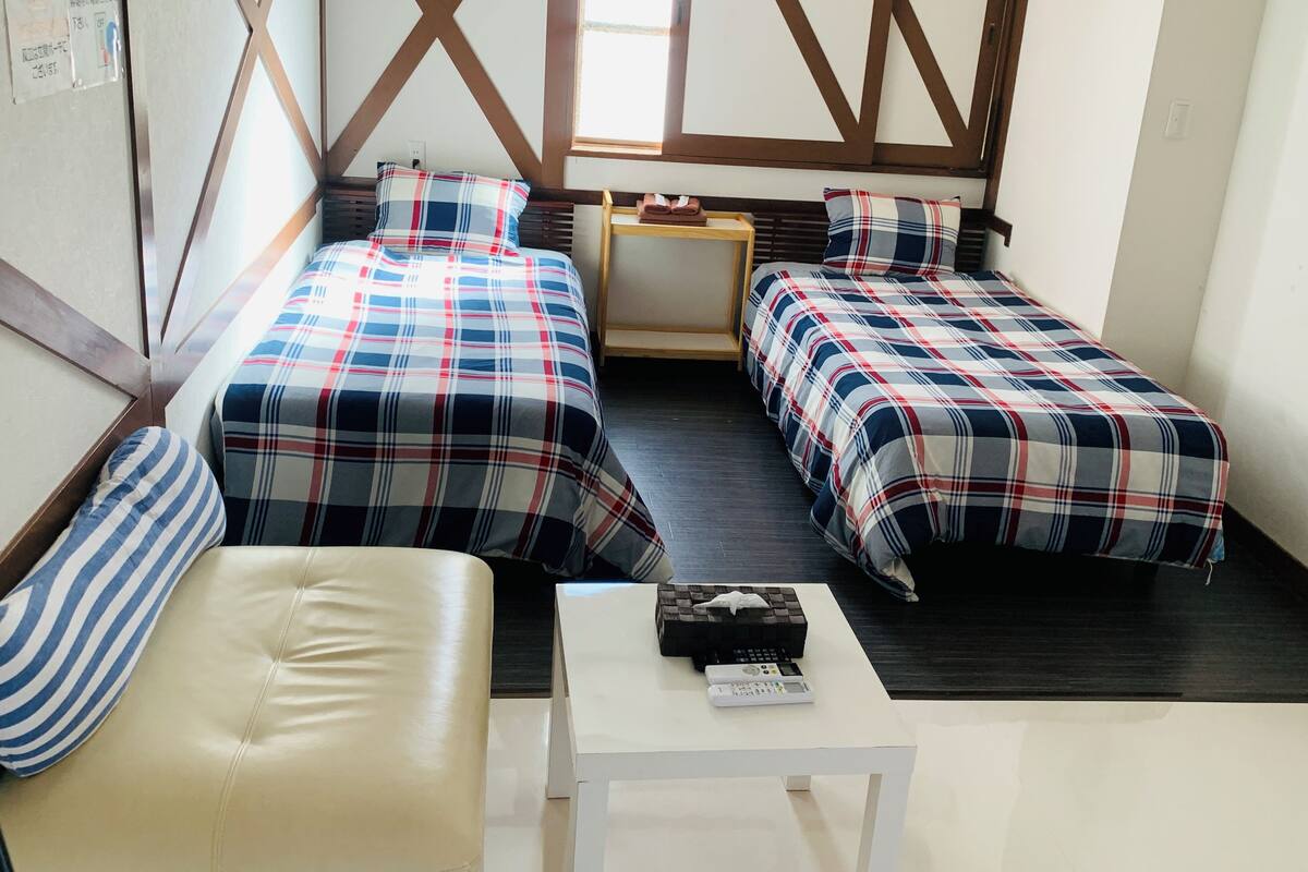A room with two beds, a small table, and a bench.