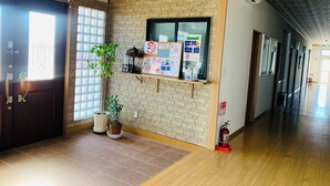 A hallway with a wooden floor, a brick wall, a fire extinguisher, and a potted plant. - villageBFH - Hostel (Omura)