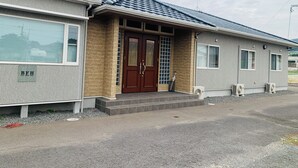 A two-story building with a tiled roof, a brick facade, and a central entrance with a wooden door. - villageBFH - Hostel (Omura)