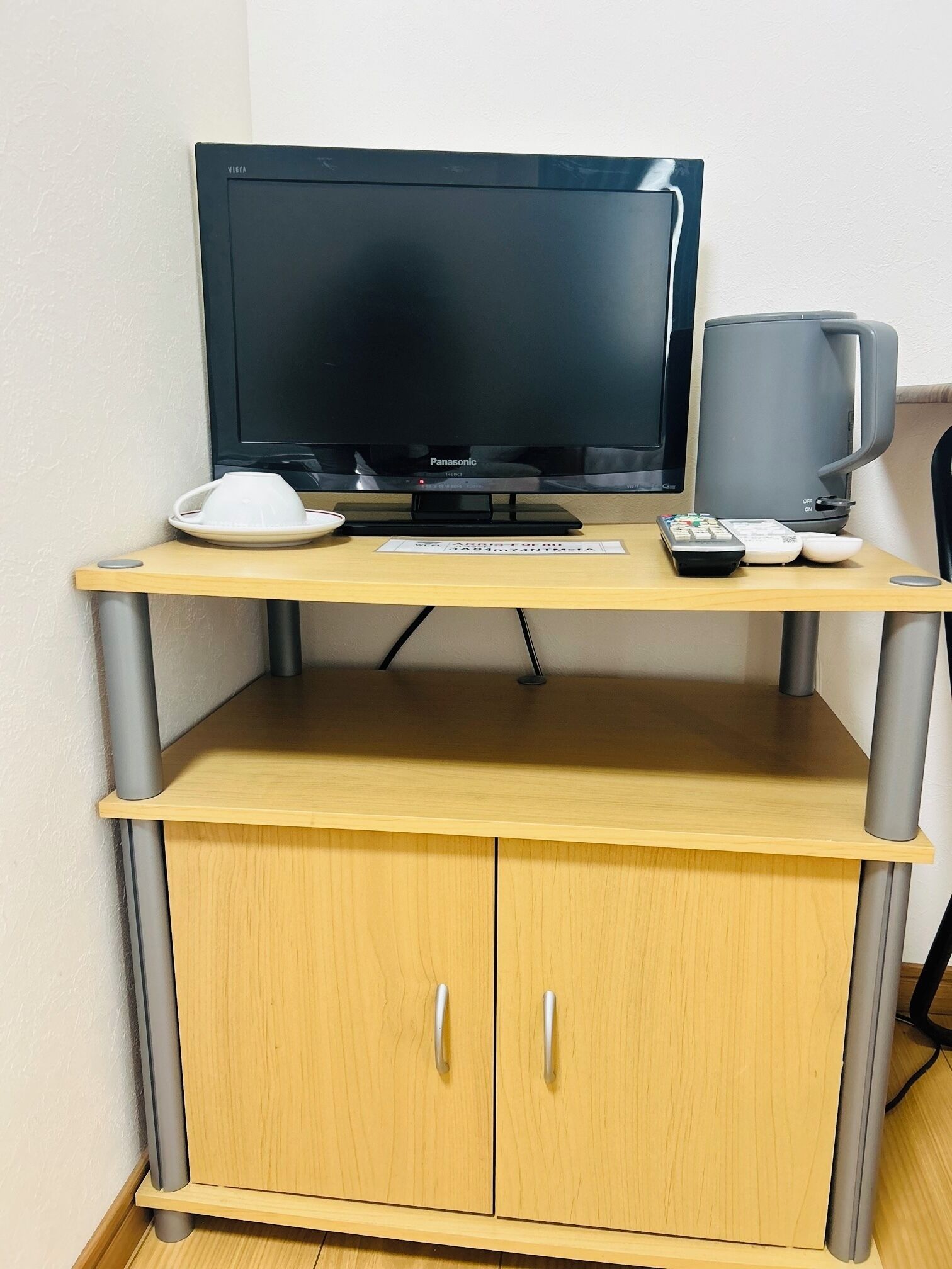 A wooden desk with a flat-screen TV, a remote control, a cup, and a smartphone.