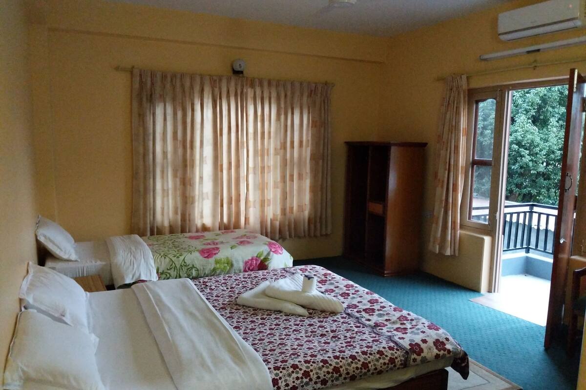 Habitación de hotel con cama, aparador de madera, ventilador de techo y vista al exterior.