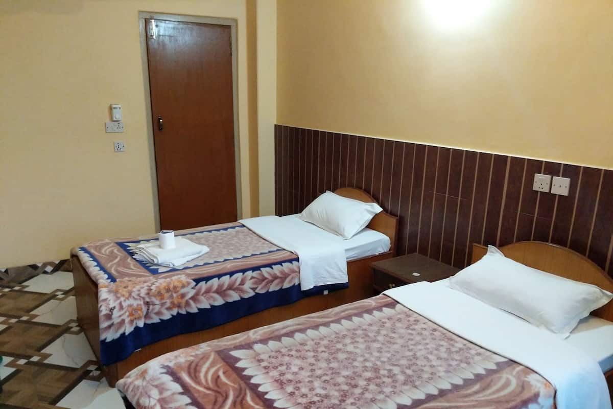 Habitación de hotel con dos camas, cada una con colcha estampada y ropa blanca. Se observa un cabecero de madera, una mesita de noche y una puerta con cerradura.