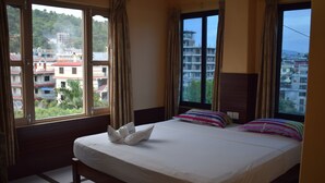Una habitación de hotel con una cama grande, dos ventanas y vista a la ciudad.