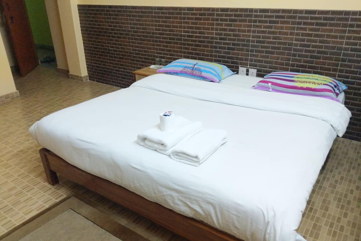 Una cama bien hecha con sábanas blancas y toallas dobladas, un cabecero de madera y una mesita de noche con una lámpara.