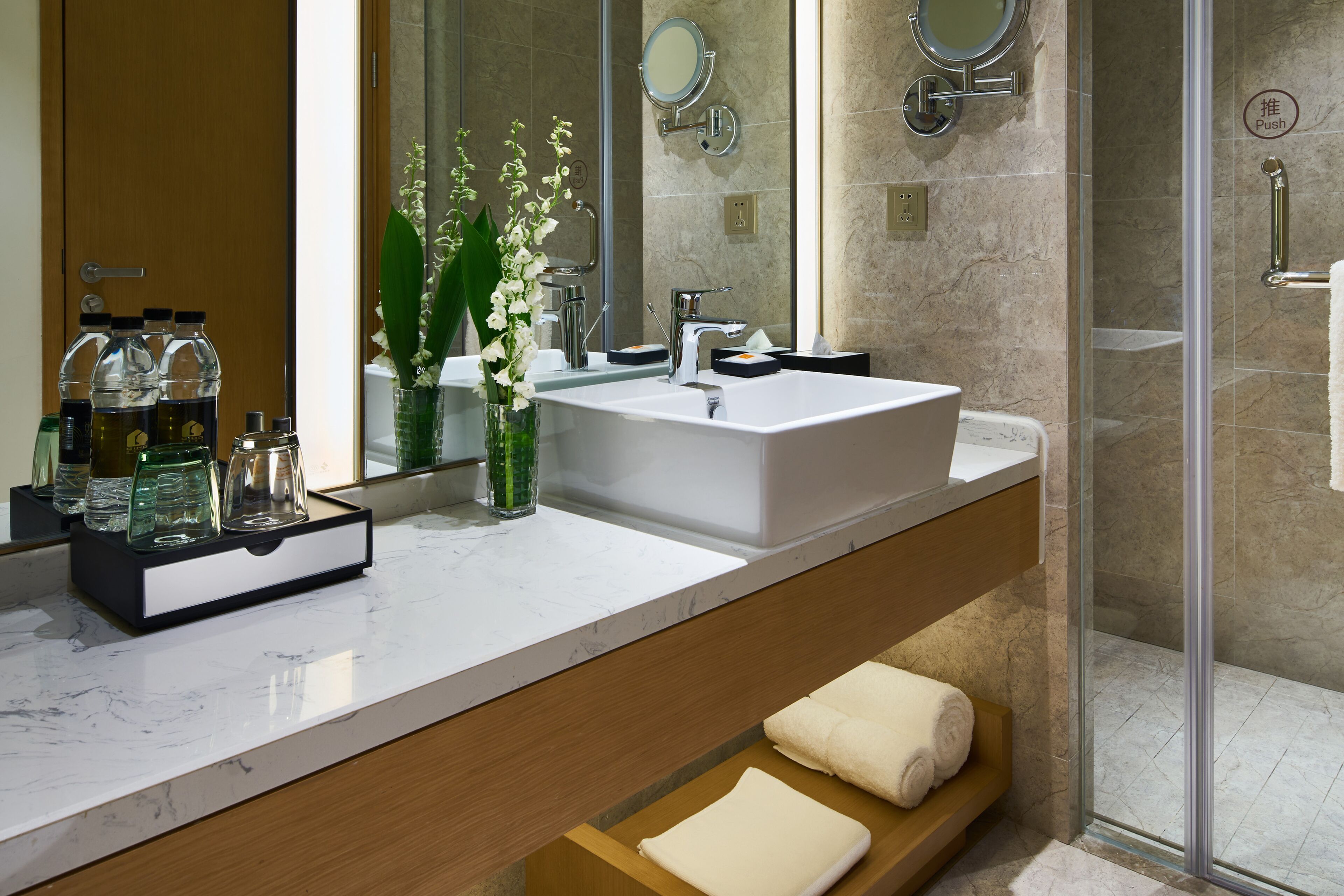 A modern bathroom with a large mirror, a white sink, and a glass shower enclosure.