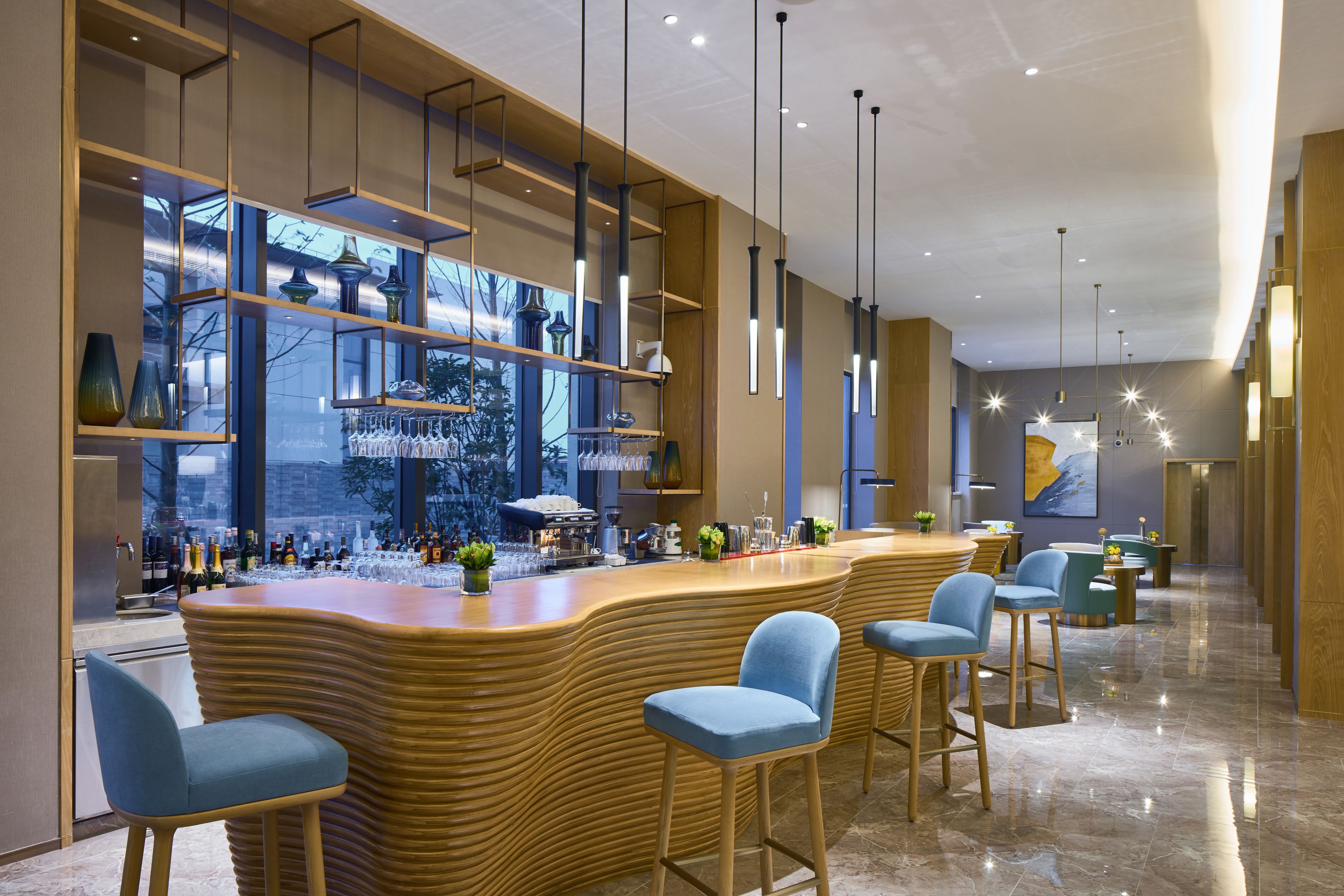 Eine moderne Bar mit einer gebogenen Holztheke, blauen Barhocker und Regalen mit Gläsern.
