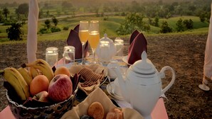 A table set for breakfast with fruits, glasses of juice, and a teapot, overlooking a scenic landscape at sunset. - Fort Dhariyawad Heritage Hotel Udaipur (Dhariyawad)