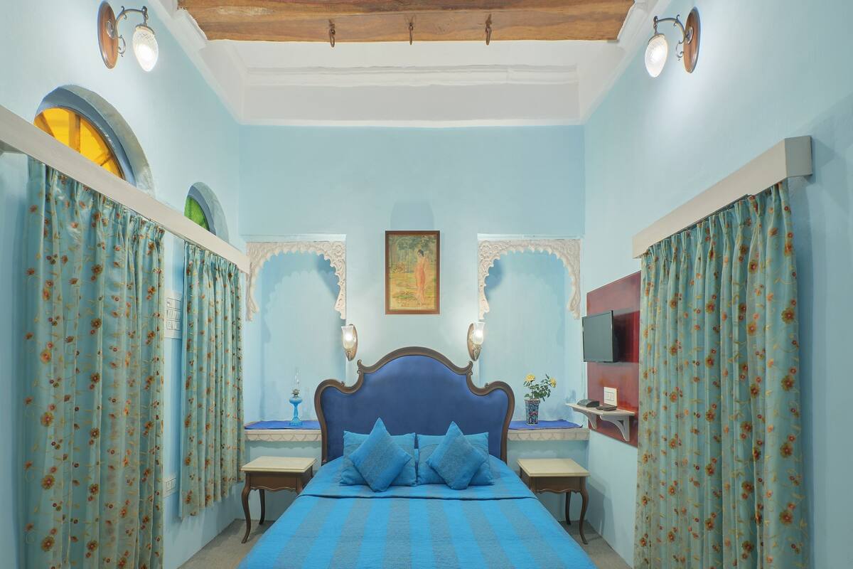 Une chambre à coucher avec un lit, des rideaux, un tableau, une télévision et une petite table.
