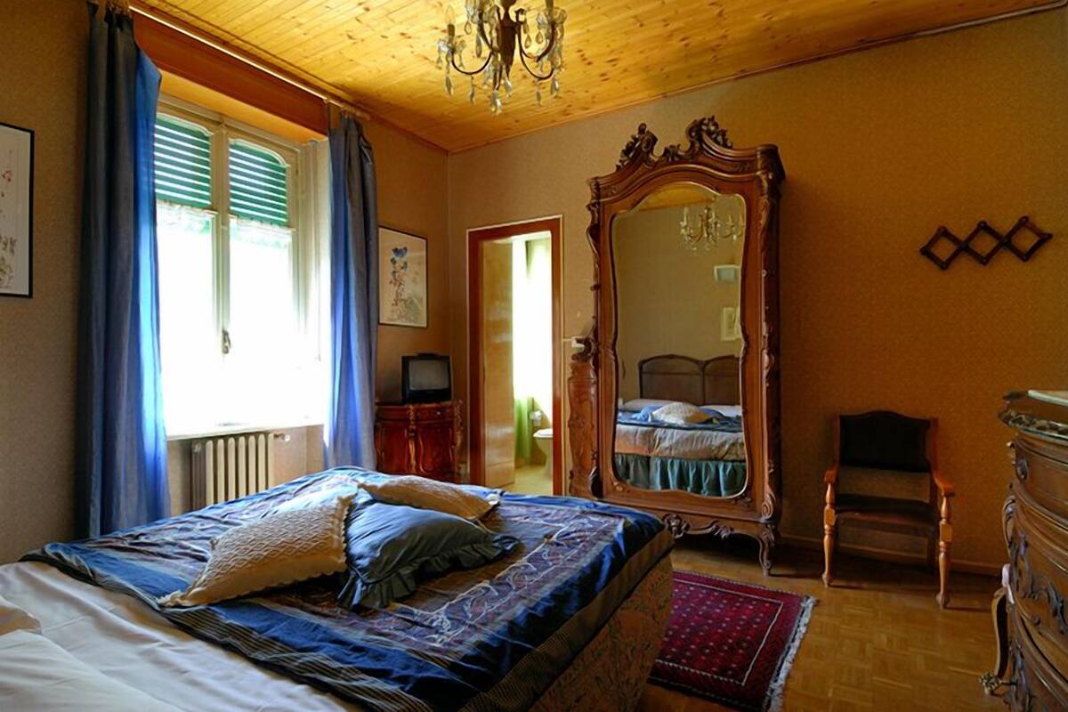 A bedroom with a large bed, a wooden dresser, a mirror, and a chandelier.