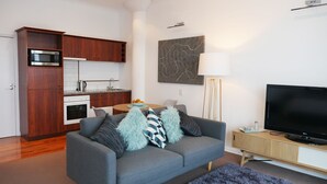 Un apartamento moderno con kitchenette, sofá gris, televisor de pantalla plana y arte abstracto en la pared.