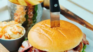 Un hamburger avec un couteau posé dessus, des frites et une salade de chou, le tout servi sur un plateau en bois.