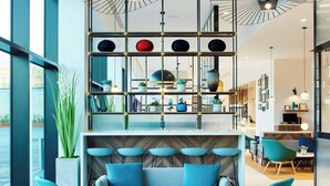 Ein modernes Interieur mit einer Sitzecke, einem dekorativen Regal mit Pflanzen und Blick durch große Fenster.