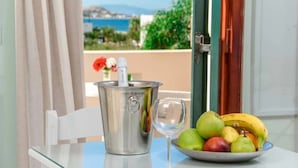 A table with a fruit bowl and a wine glass, a metal container, and a view of the sea and buildings. - Plaka Hotel I (Naxos)