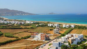 A coastal residential area with modern white buildings, a clear blue sea, and a hilly landscape in the background. - Plaka Hotel I (Naxos)