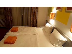 A hotel room with two beds, a radiator, curtains, and a wall-mounted lamp. - Gasthof Franziska (Stuttgart)