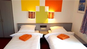 A hotel room with two beds, each with white linens and orange towels. There are wall-mounted lamps with wooden shades, and a control panel on the wall. - Gasthof Franziska (Stuttgart)
