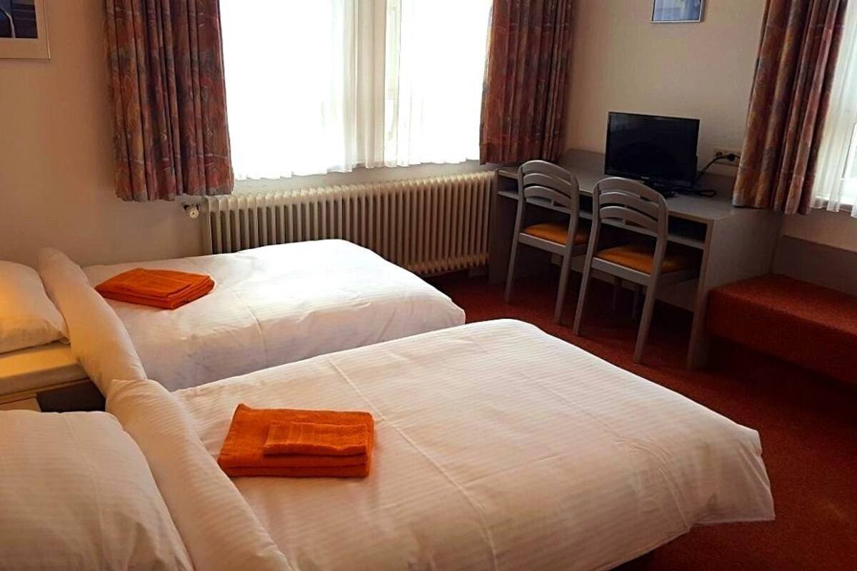 A hotel room with two beds, a desk with a chair, a television, and a window with curtains.