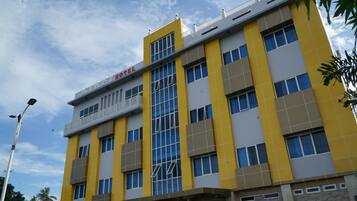 A multi-story hotel with a yellow and grey facade, large windows, and a visible balcony on the upper floor.