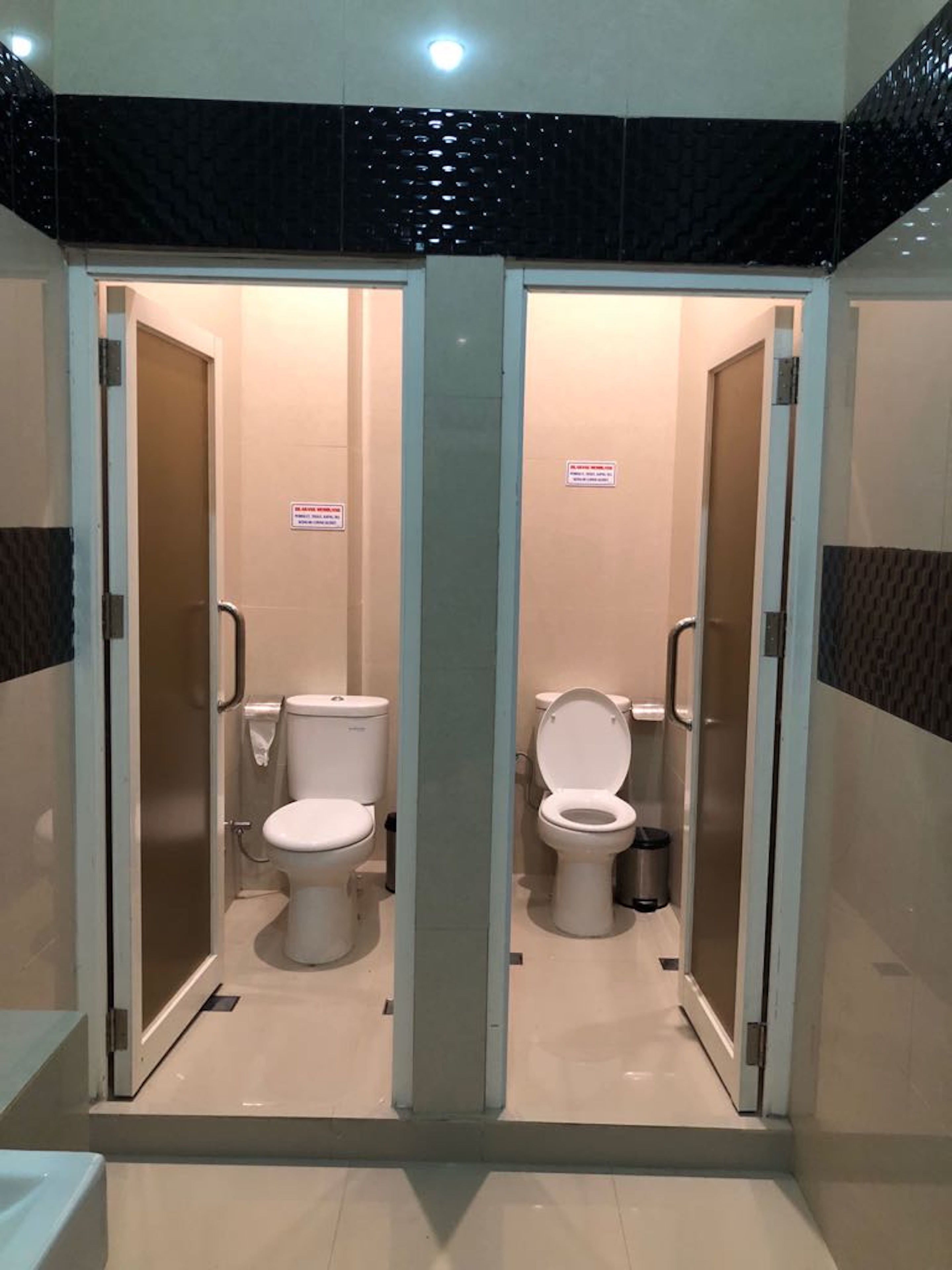 A restroom with two toilets, each with a privacy partition and a handrail.