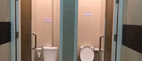 A restroom with two toilets, each with a privacy partition and a handrail.