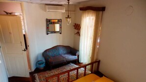 A bedroom with a bed, a sofa, a mirror, and a window with curtains. - Taksiyarhis Pension (Ayvalik)