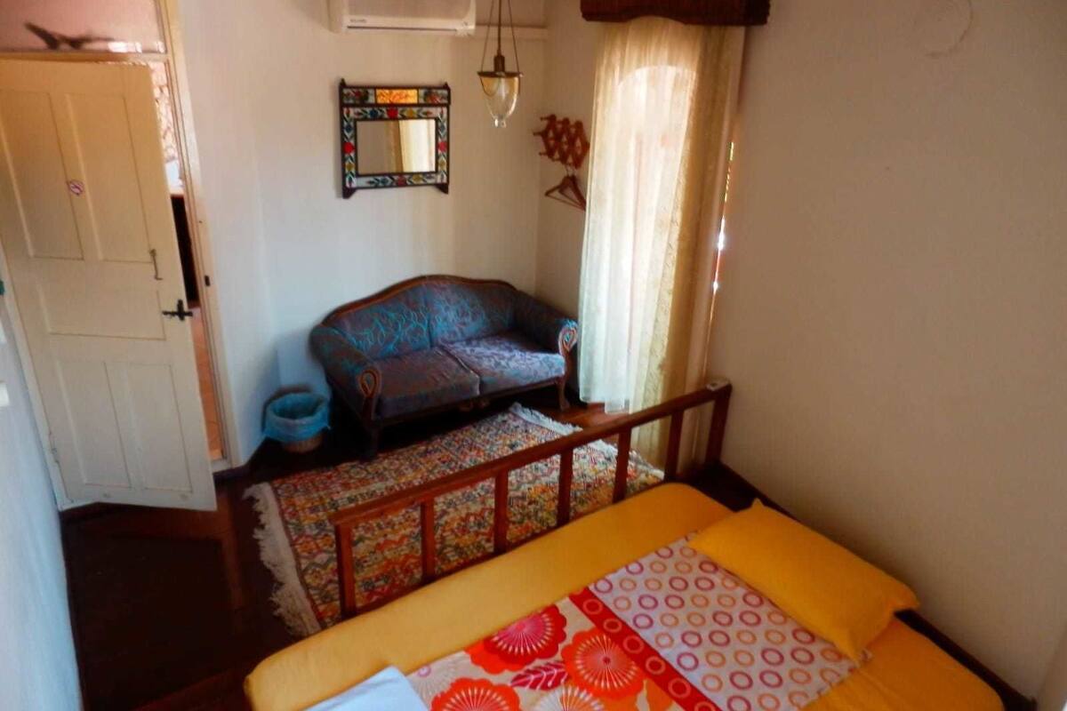 Um quarto com cama, sofá, espelho e janela com cortinas.