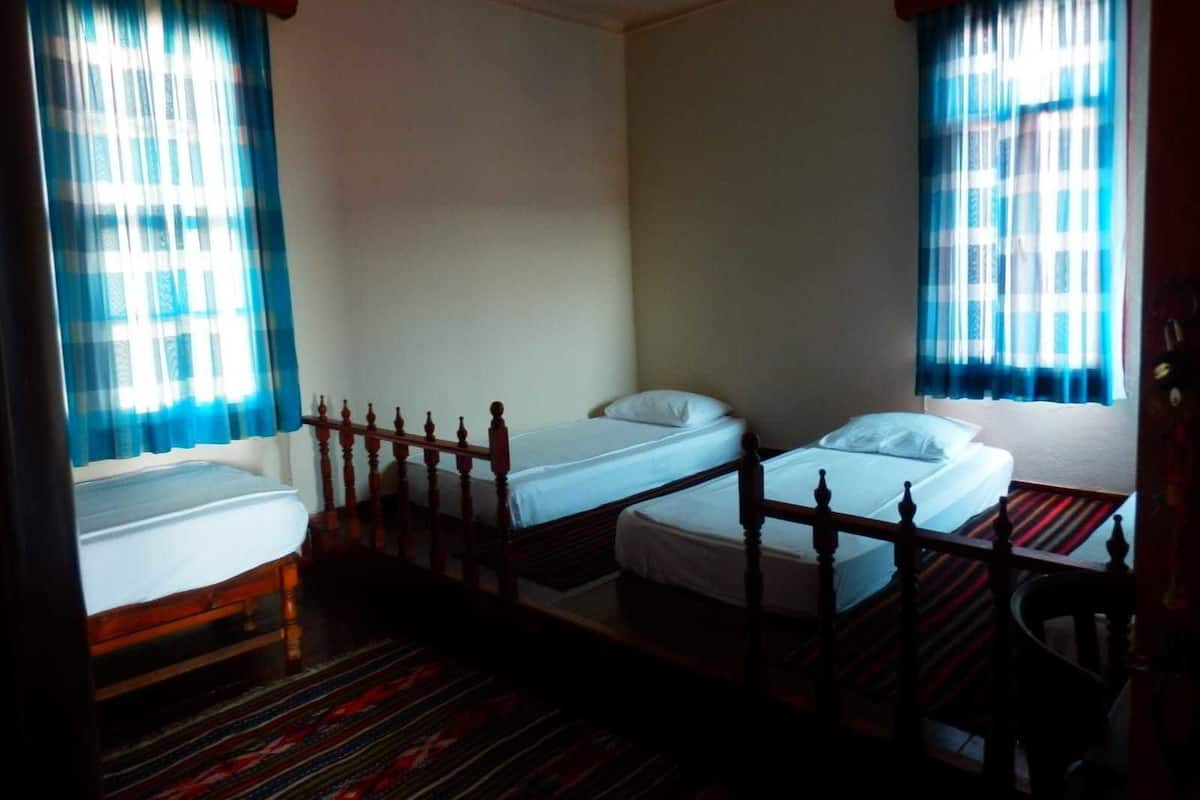 Quarto com três camas de solteiro, cabeceiras de madeira e carpete estampado.