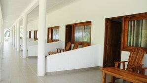 Ein Korridor mit weißen Säulen, hölzernen Bänken und fensterartigen Öffnungen mit Vorhängen.