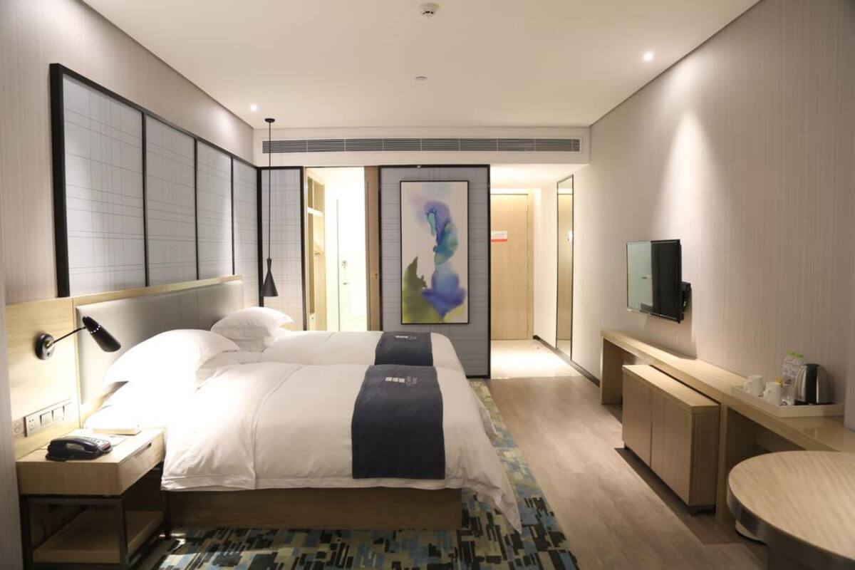 A modern hotel room with a large bed, bedside table, lamp, and a TV on a stand.