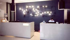 A reception area with two white reception desks, a dark blue wall with illuminated geometric patterns, and a person seated at one of the desks. - Echarm Hotel Kecun Pazhou (Guangzhou)