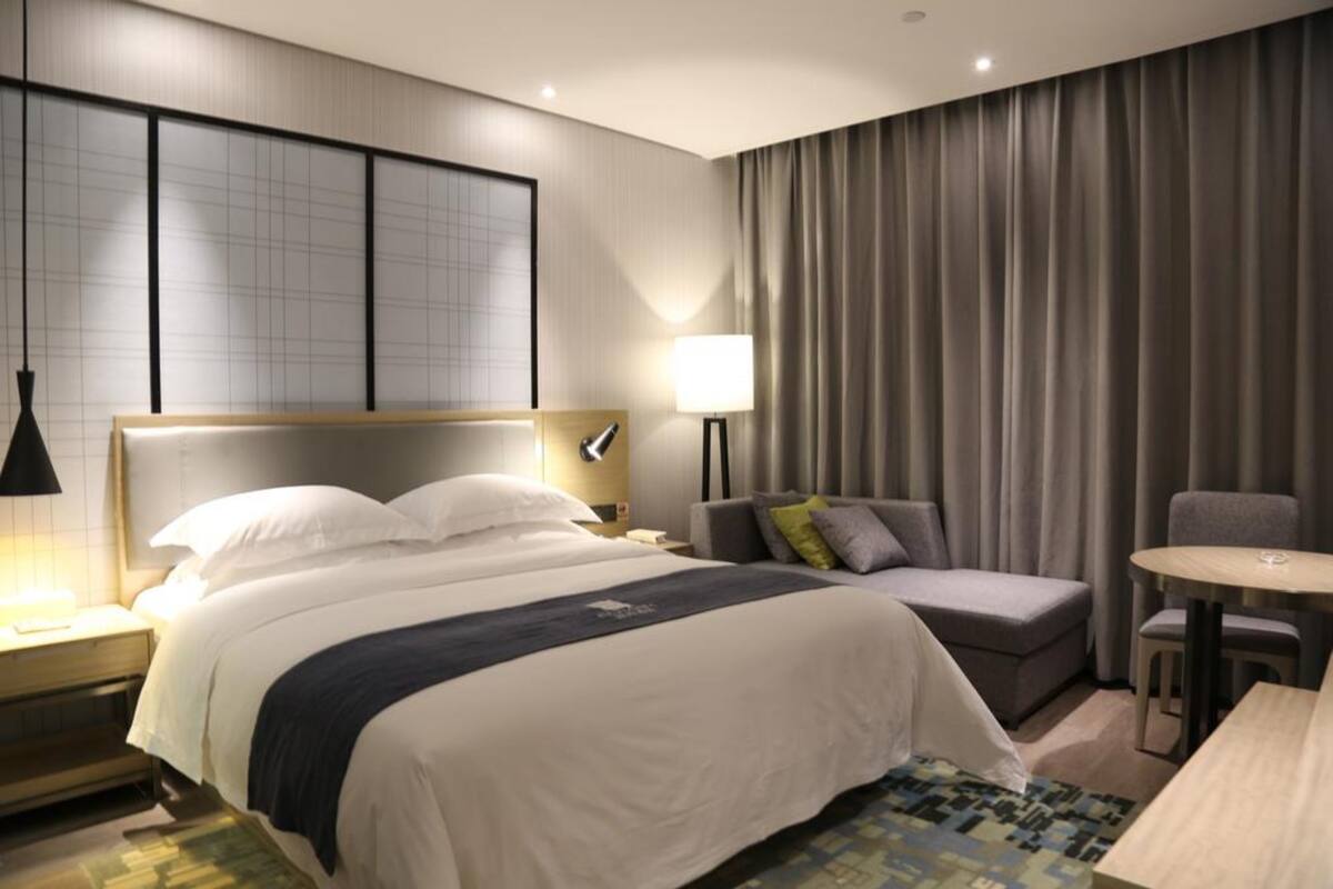 A hotel room with a large bed, a sofa, a small table, and a lamp.