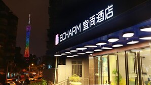 A hotel with a prominent sign, a modern facade, and a view of a tall, illuminated tower in the background. - Echarm Hotel Kecun Pazhou (Guangzhou)