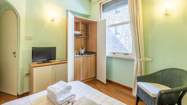 A room with a bed, a television, a kitchenette, and a window with curtains. - Tiny Ponte Vecchio by Mmega (Florence)