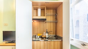 A compact kitchen with wooden cabinets, a built-in oven, a sink, and a window with a view of a building. - Tiny Ponte Vecchio by Mmega (Florence)