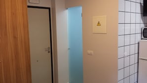 A room with a wooden door, a blue door, and a tiled wall with a warning sign. - Hostal Usera (Madrid)