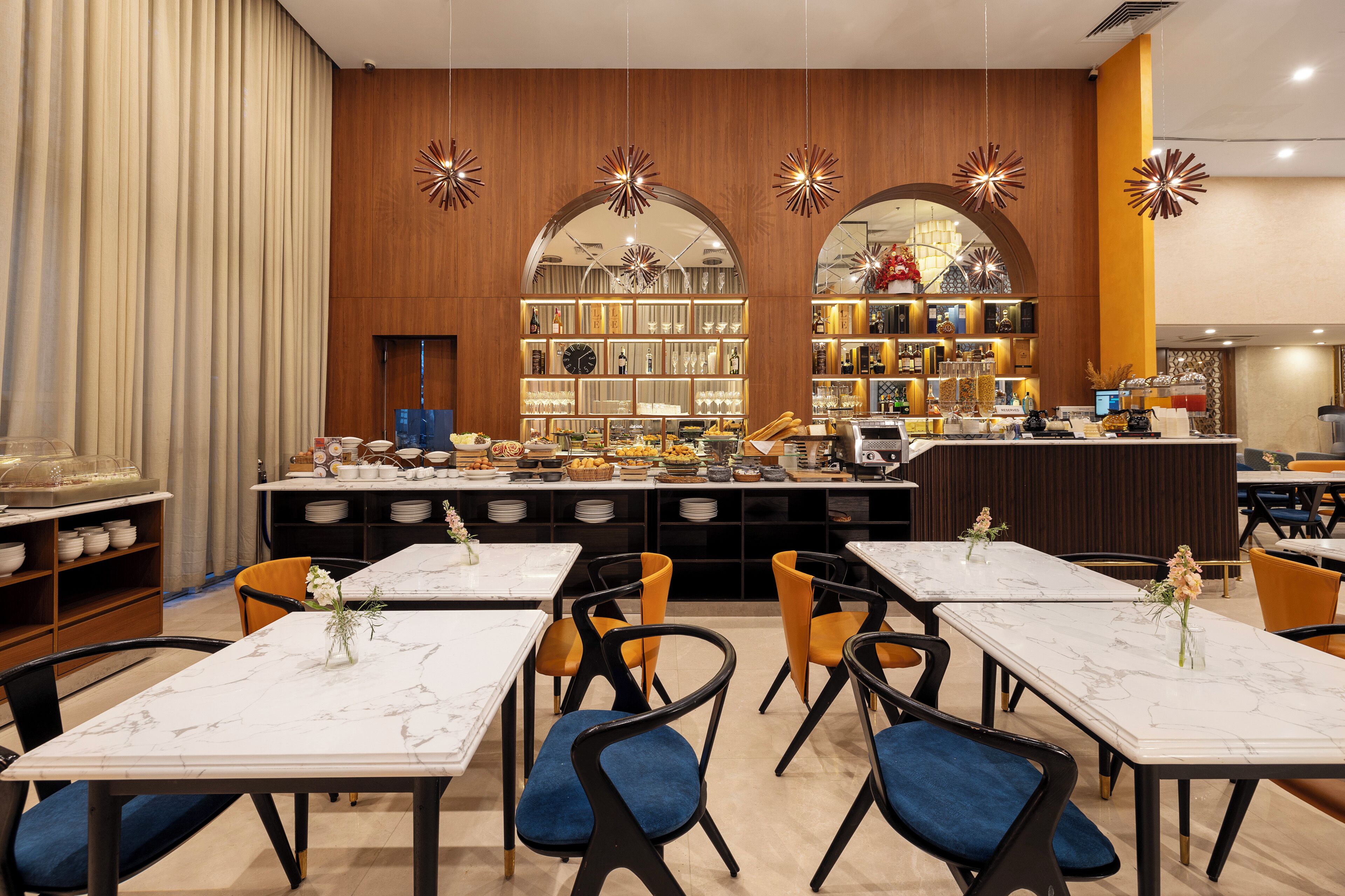 A restaurant with marble tables, blue cushioned chairs, and a central buffet area.