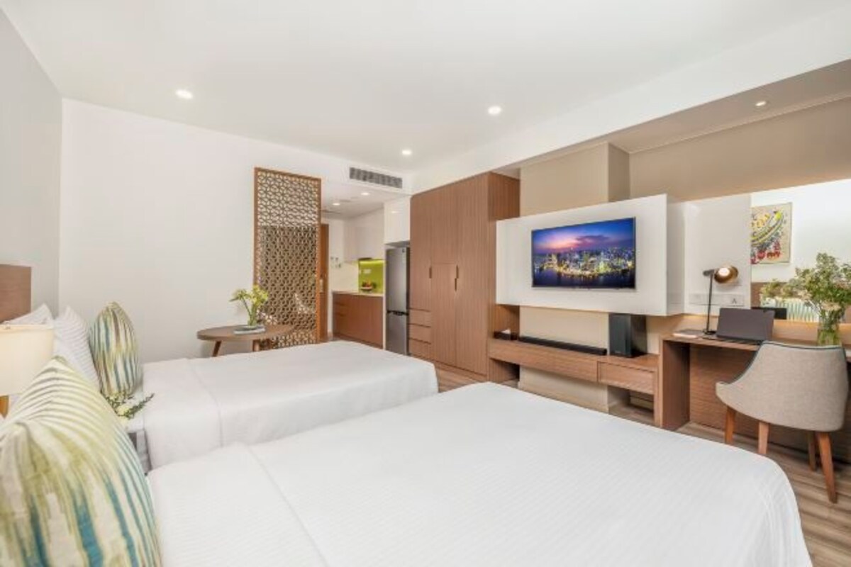A hotel room with two beds, a TV, a desk, and a chair.