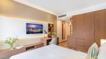 Una habitación de hotel moderna con una cama grande, un escritorio con una computadora portátil, un televisor montado en la pared y un armario de madera.