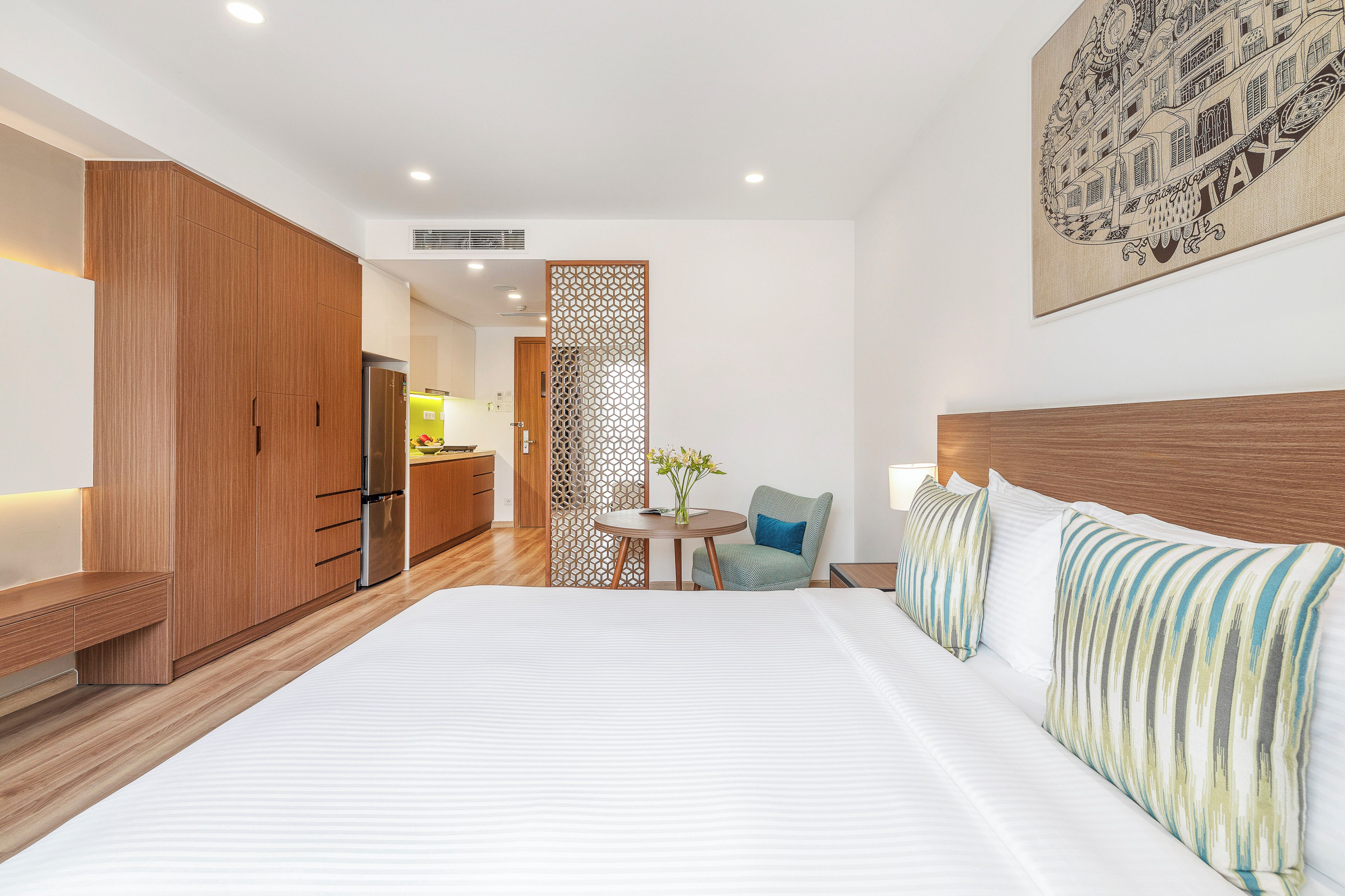 Una habitación de hotel moderna con una cama grande, un armario de madera, una pequeña mesa de comedor con una silla y un adorno en la pared.