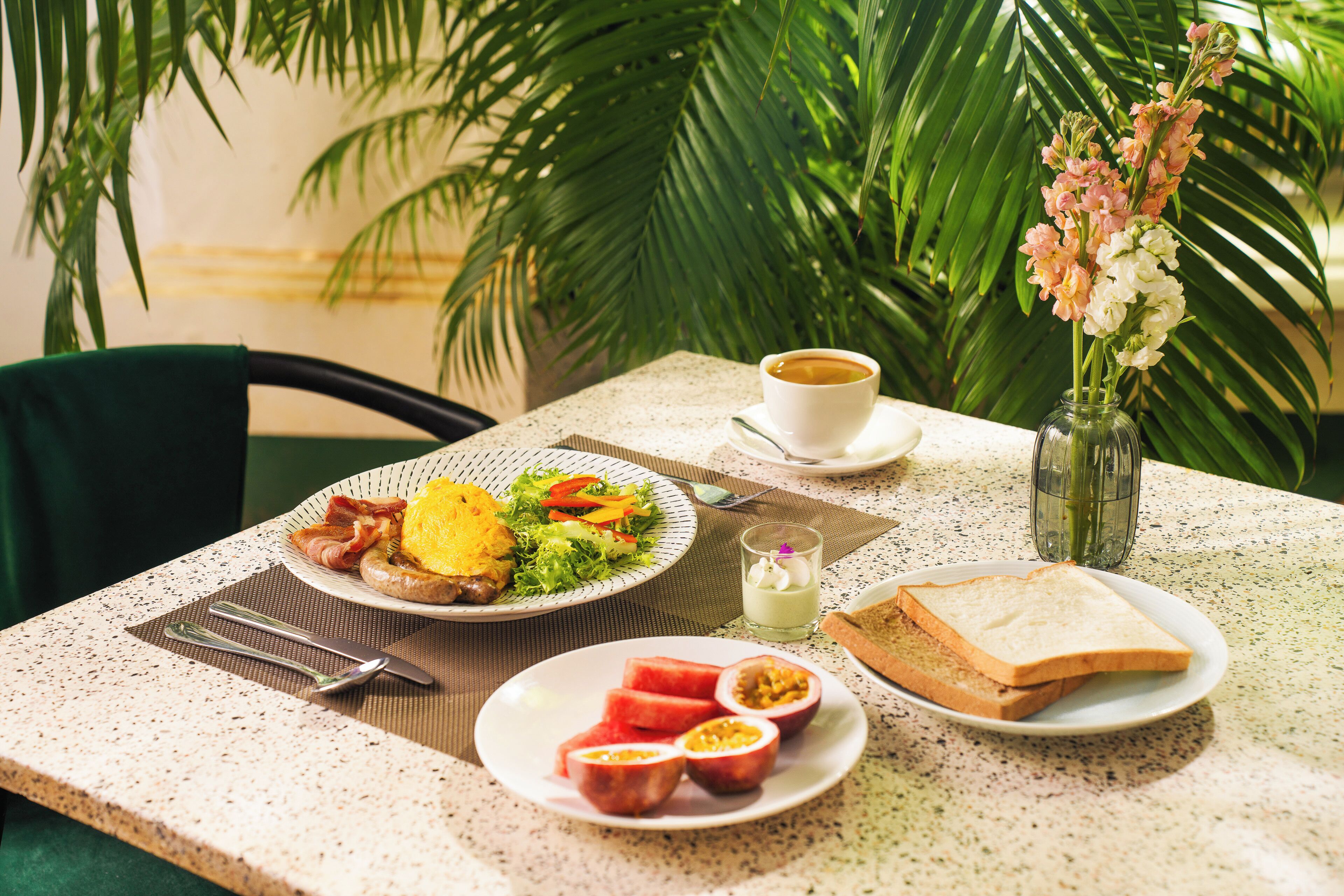 A breakfast table with plates of food, a cup of coffee, and a vase of flowers.