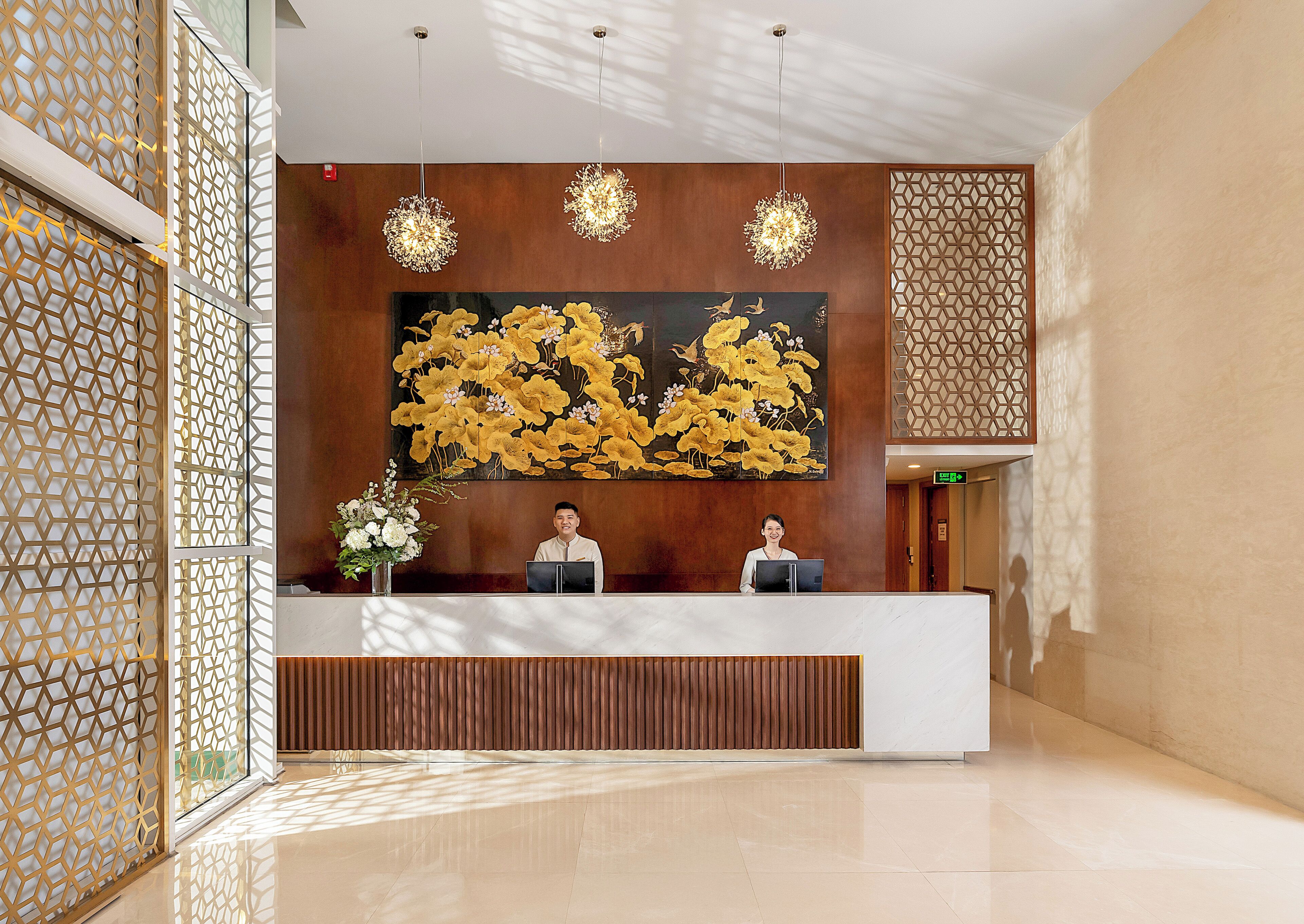 A reception area with a wooden reception desk, two receptionists, a large floral painting, and decorative lighting.
