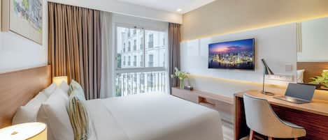 A hotel room with a bed, desk, chair, and a large window with curtains.