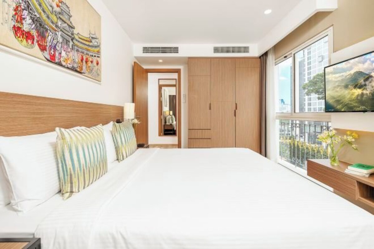 A hotel room with a large bed, a TV mounted on the wall, and a view of the city through the window.