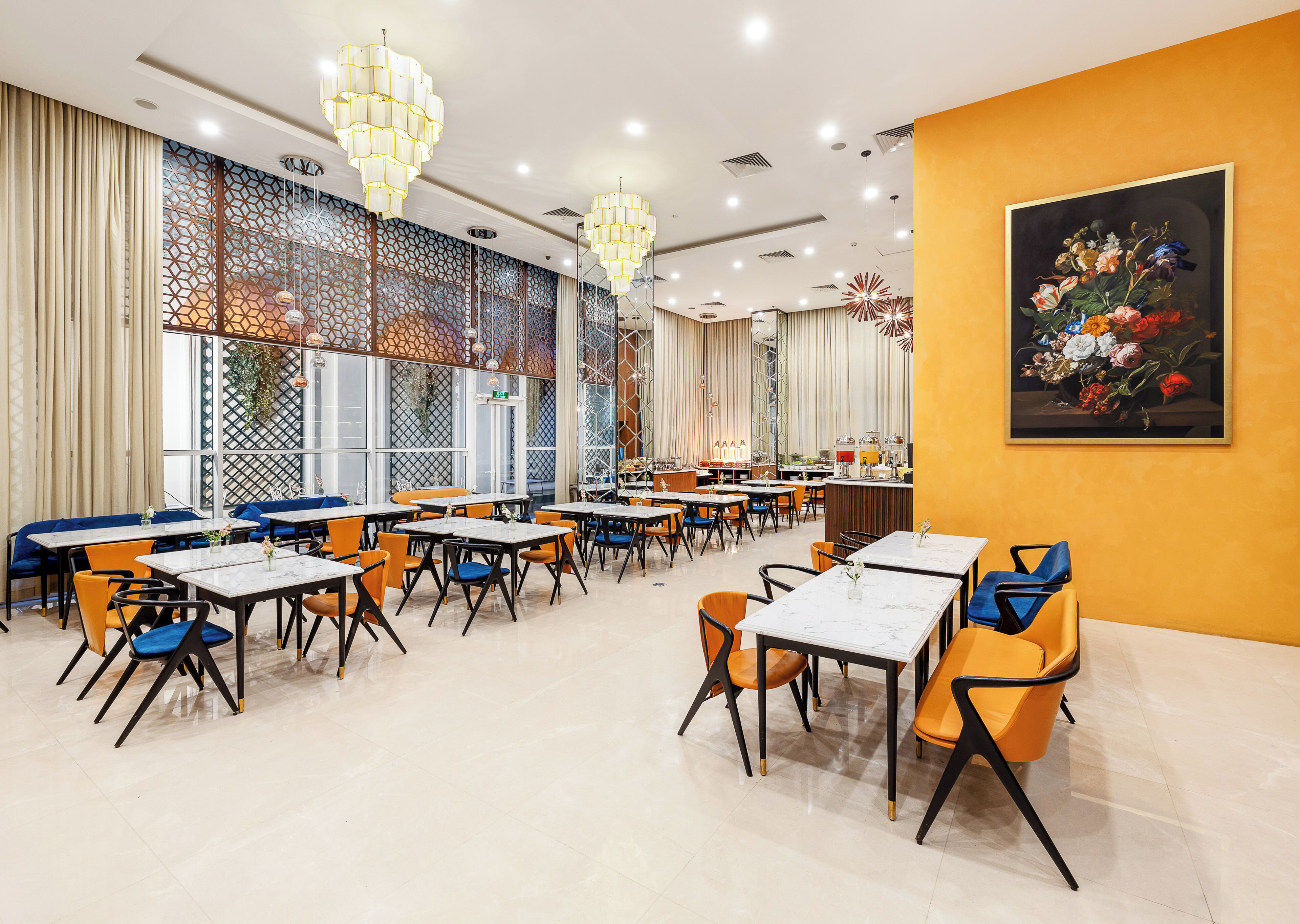 A restaurant with multiple tables and chairs, a decorative wall with a painting, and a patterned window design.