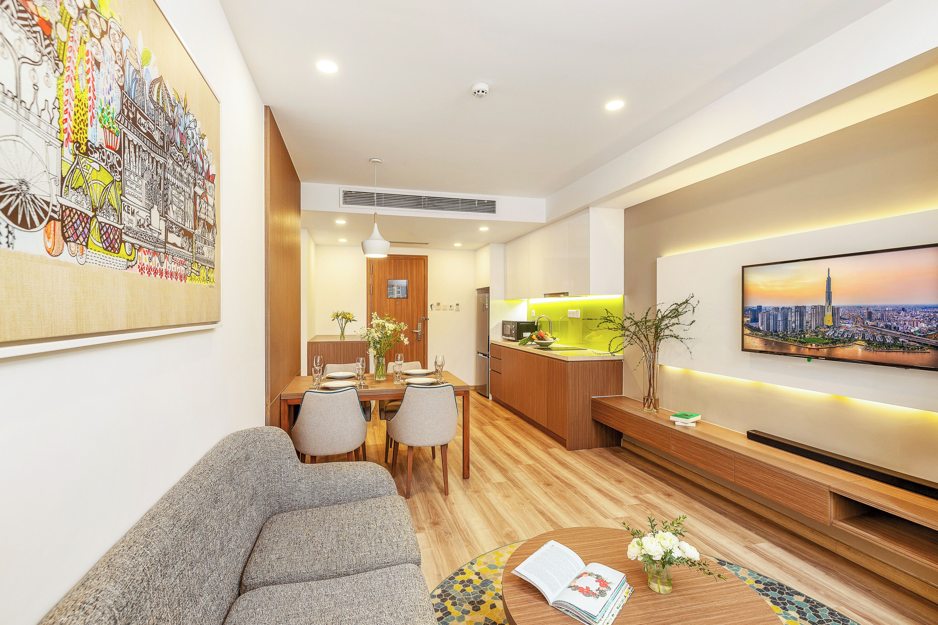 A modern living room with a sofa, dining area, kitchen, and a large painting on the wall.