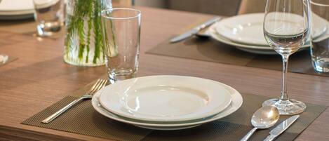 Una mesa de comedor preparada con platos, cubiertos y un florero.