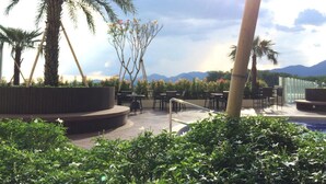 An outdoor seating area with tables and chairs, surrounded by greenery and palm trees, overlooking a mountainous landscape. - Merton Residence Ipoh (Ipoh)