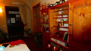 A cozy room with a wooden cabinet filled with jars and a small plant. There is a table with a red cloth and a few books. - Agritur La Gemma (Sant'Orsola Terme)