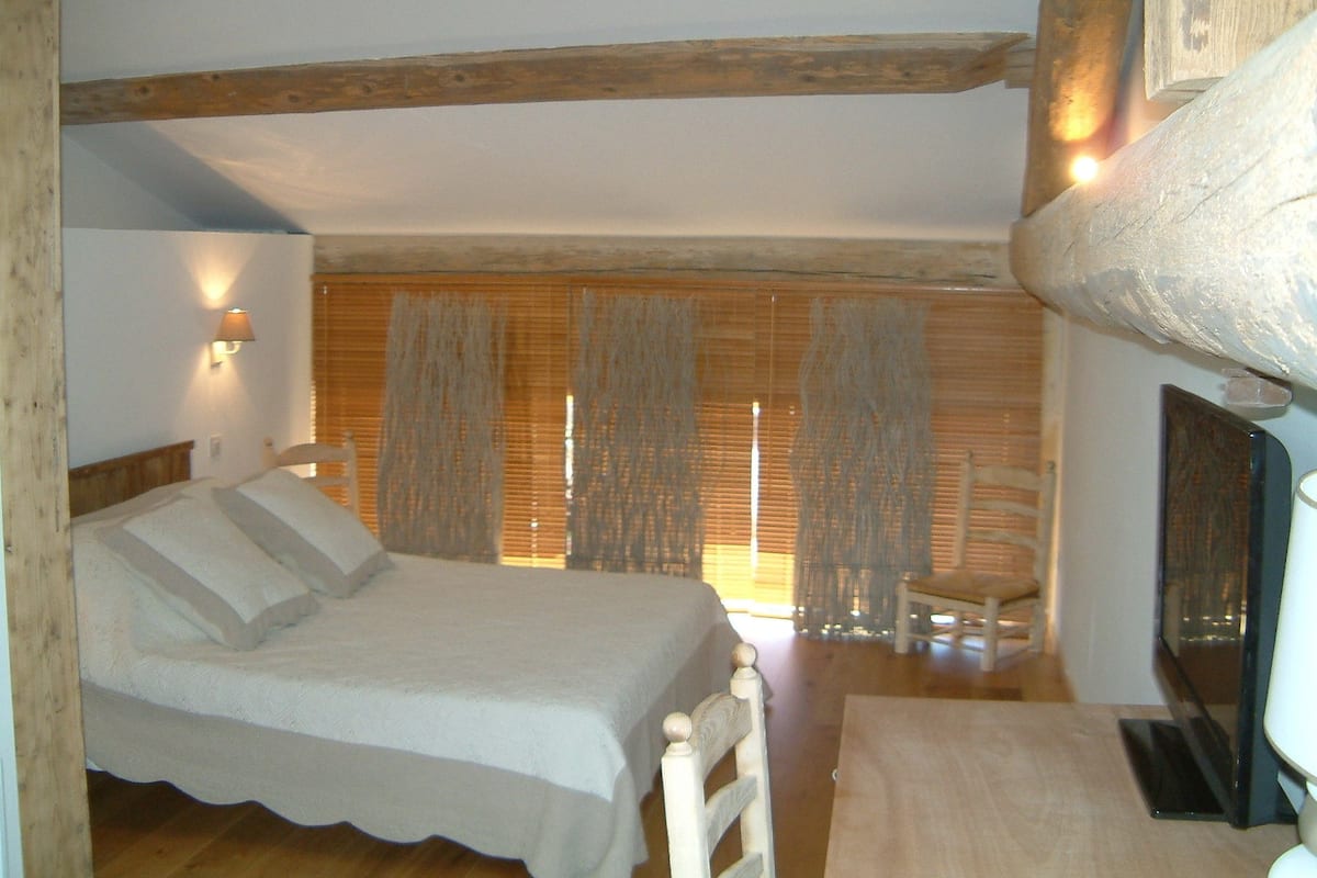 Ein Schlafzimmer mit Bett, Stuhl, Holzboden und einem Fenster mit Vorhängen.