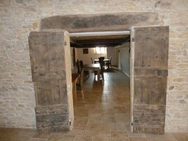 Una habitación con paredes de piedra y una rústica puerta de madera que da a un comedor con una mesa y sillas.